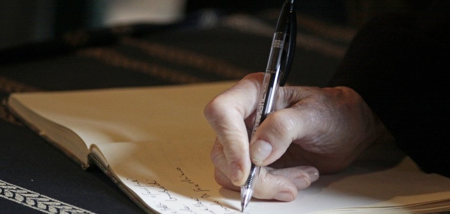 Auf dem Bild sieht man eine Hand, die ein Dokument unterschreibt.