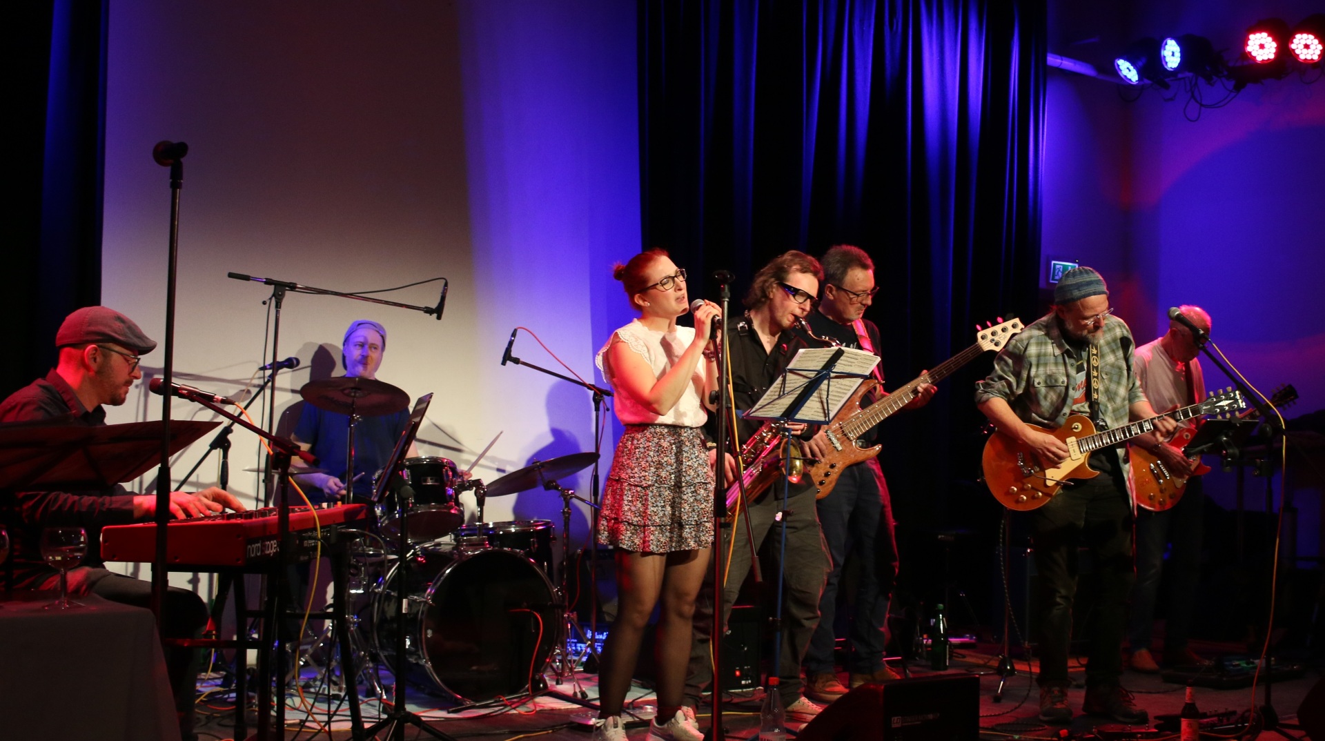 Man sieht eine Band die Instrumente spielt und eine Frau die singt.