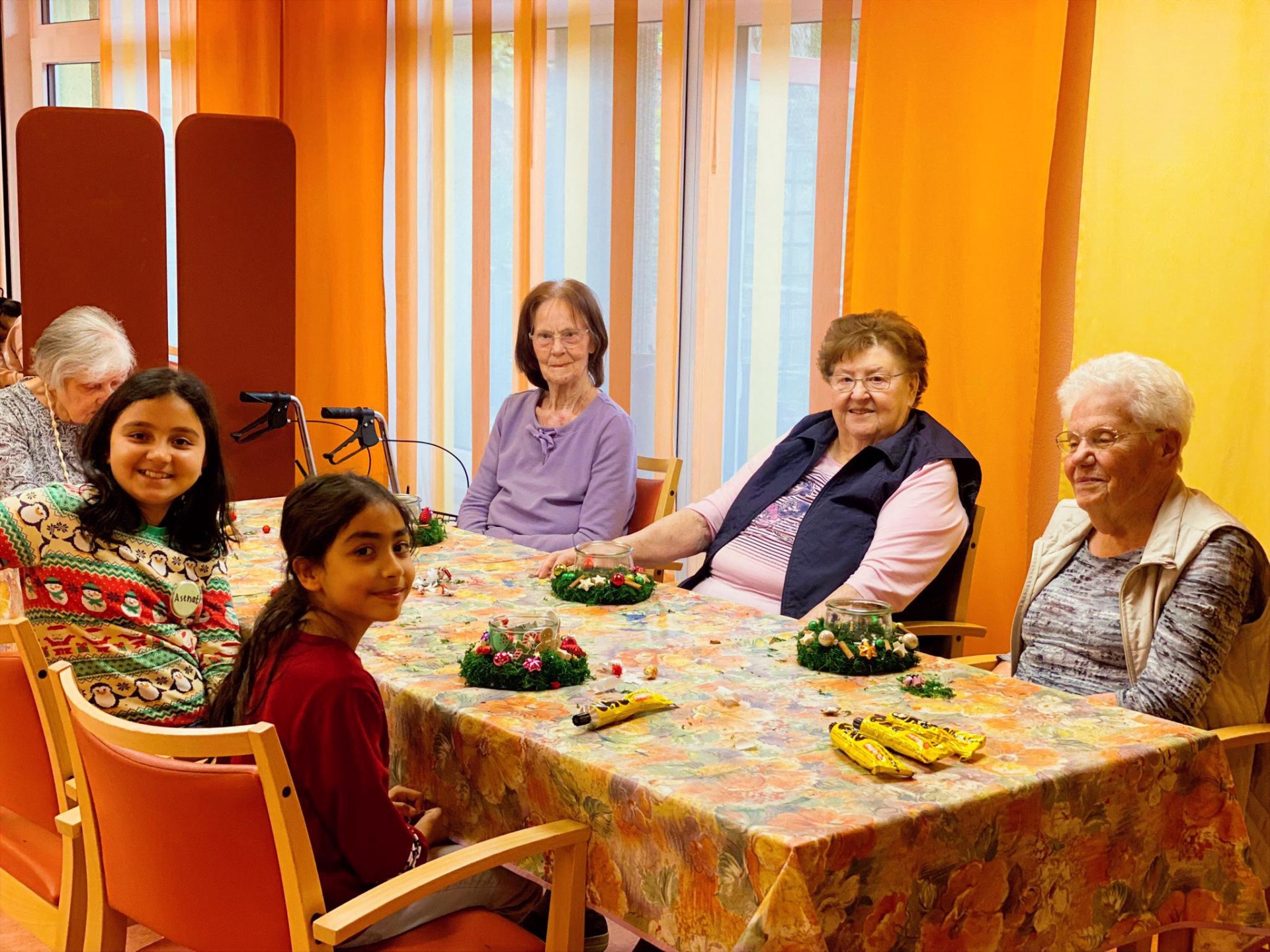 Kinder besuchen Senioren im Altersheim, sitzen an einem Tisch