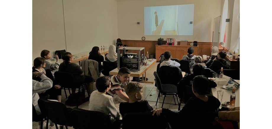Mehrere Personen sitzen vor einer Leinwand und schauen einen Film