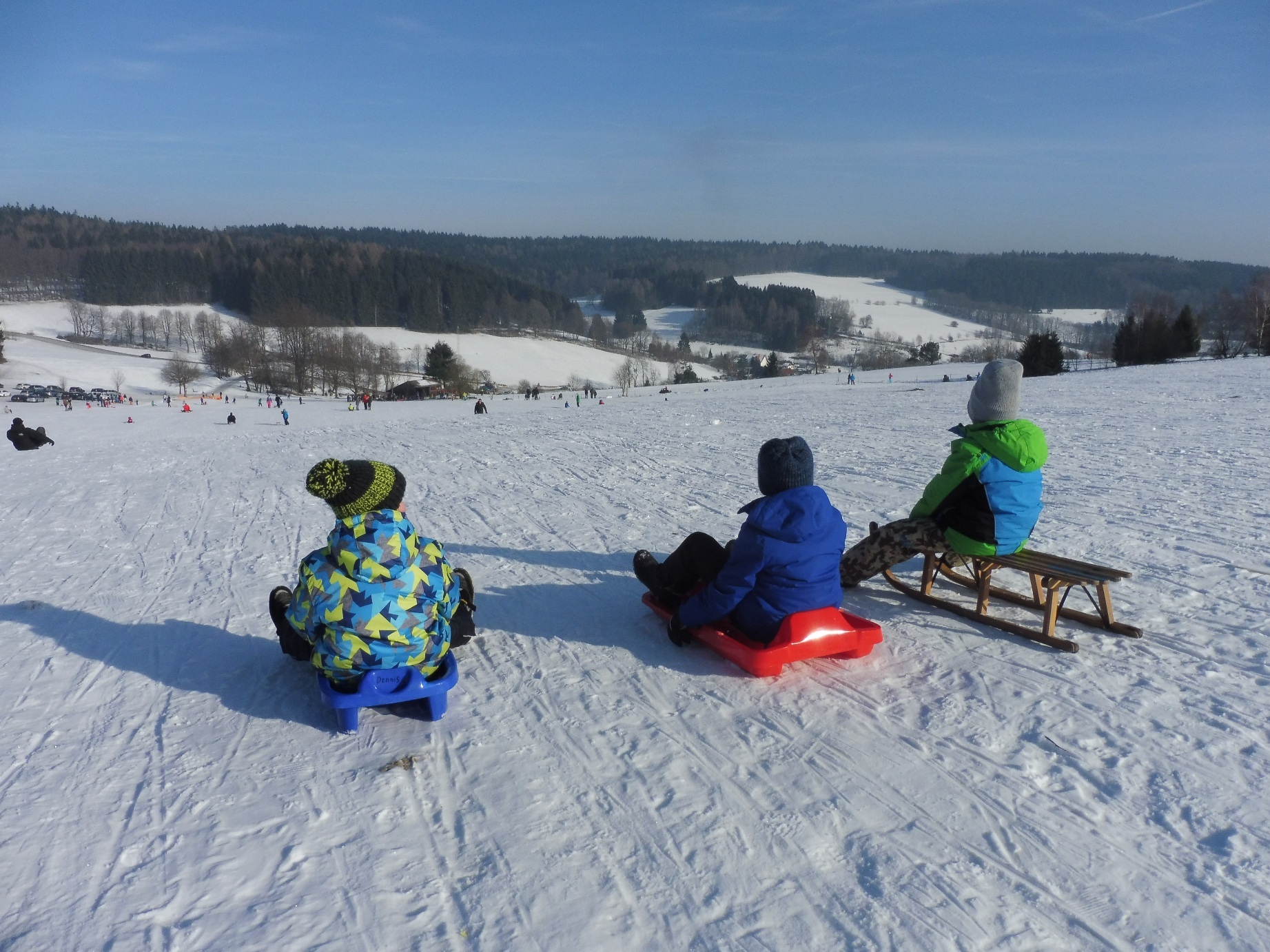 3 Personen auf einem Schlitten auf einem Hügel im Schnee