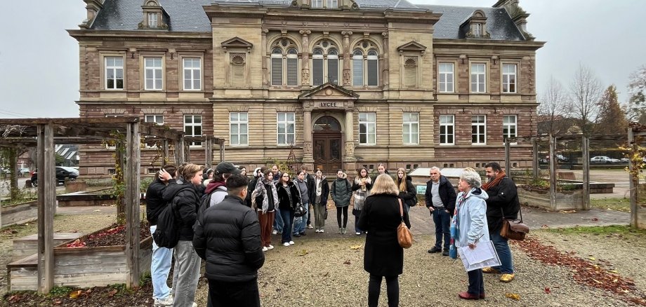 Man sieht eine Gruppe von Menschen, die in einem Kreis aufgestellt vor einem Gebäude stehen.