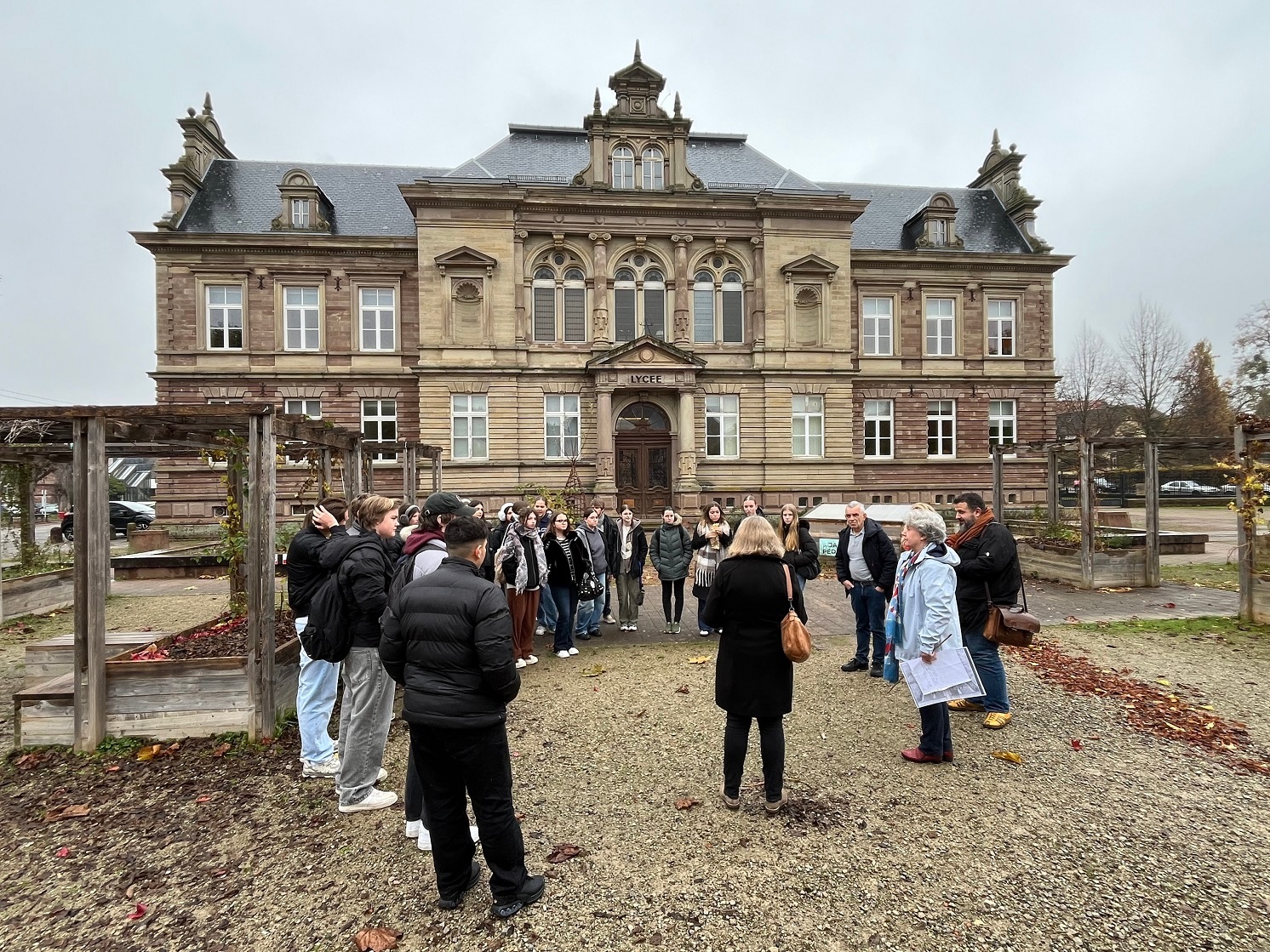 Man sieht eine Gruppe von Menschen, die in einem Kreis aufgestellt vor einem Gebäude stehen.