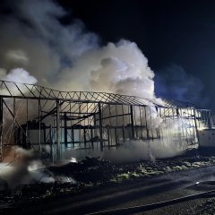 Man sieht eine abgebranntes Gewächshaus mit ganz viel Rauch im Hintergrund. 