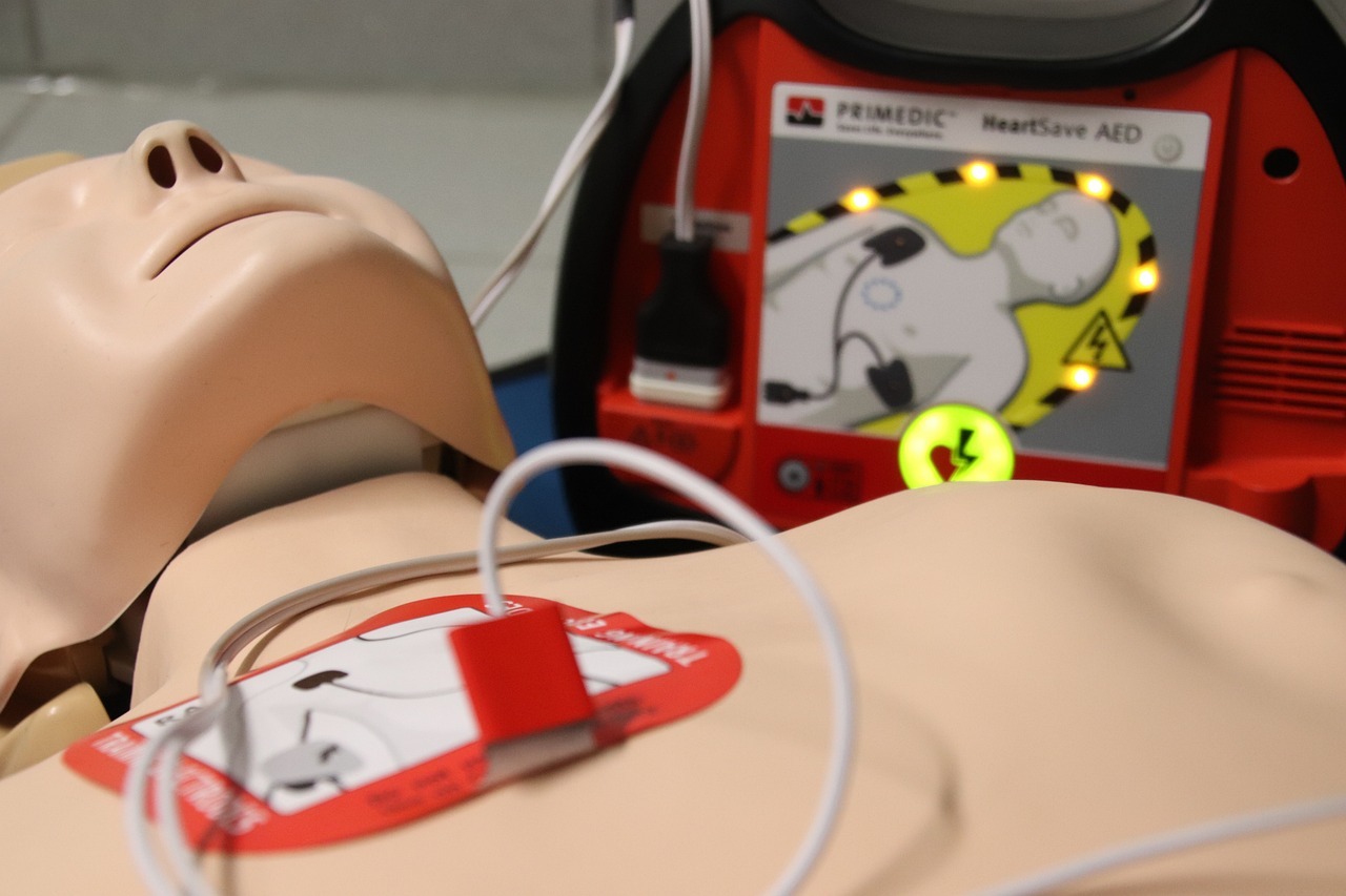 Man sieht eine Übungspuppe und einen Defibrillator.