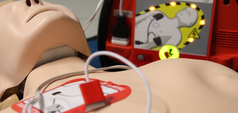 Man sieht eine Übungspuppe und einen Defibrillator.