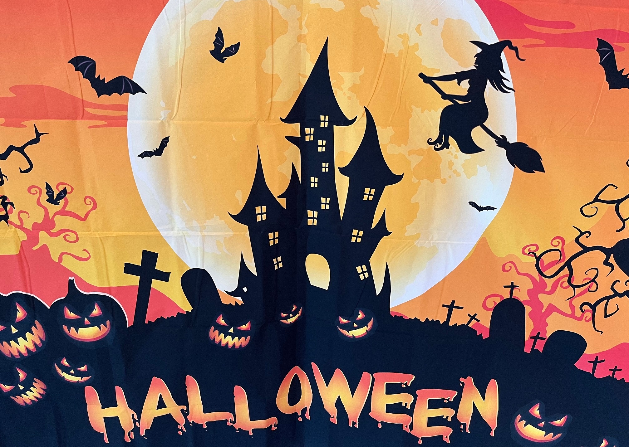 Auf dem Bild sieht man einen großen Mond, Hexenhäuser, einen Friedhof und eine Hexe auf ihrem Besen