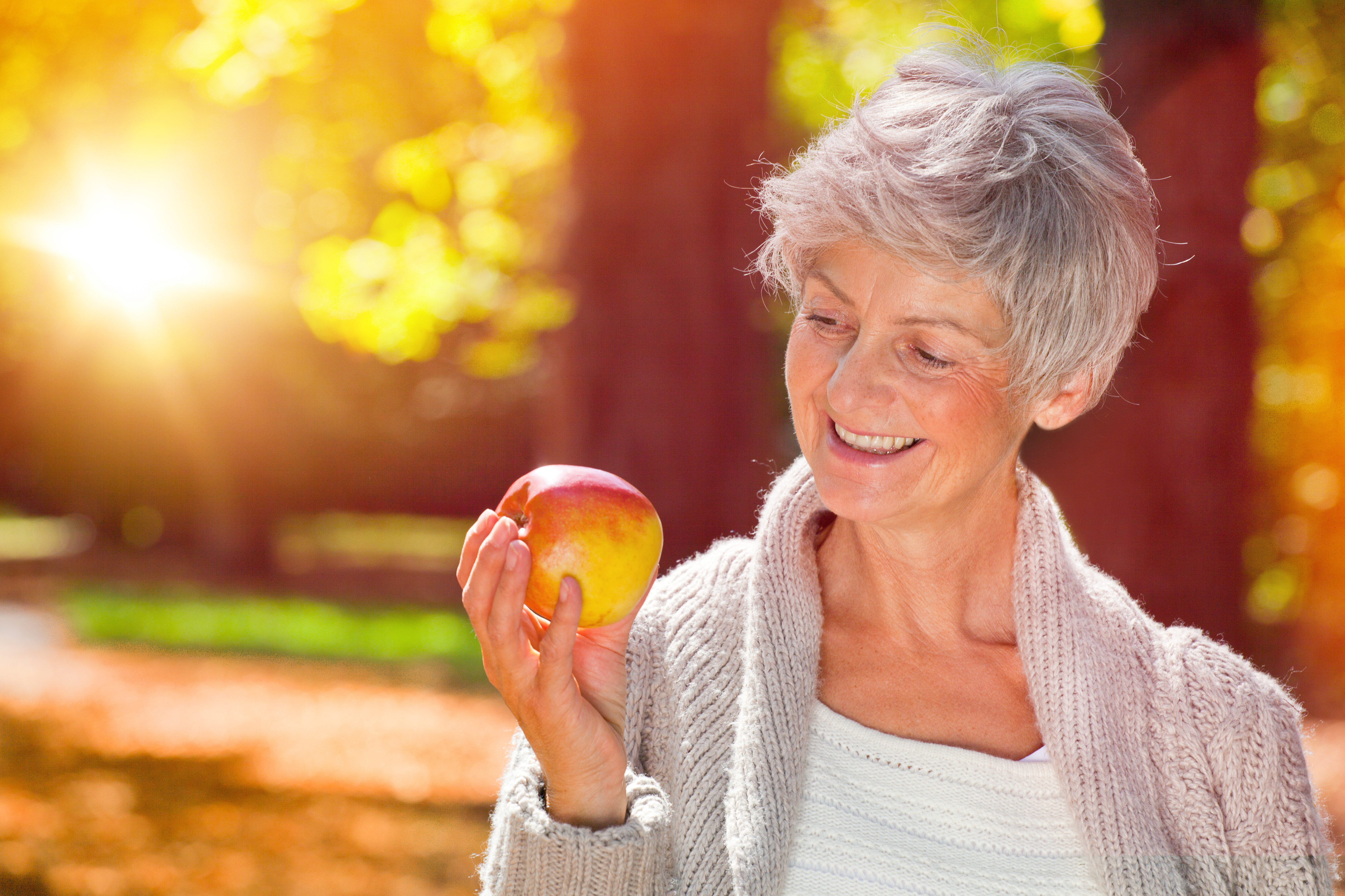 Auf dem Bild sieht man eine lachende Frau, die einen Apfel in der Hand hält. 
