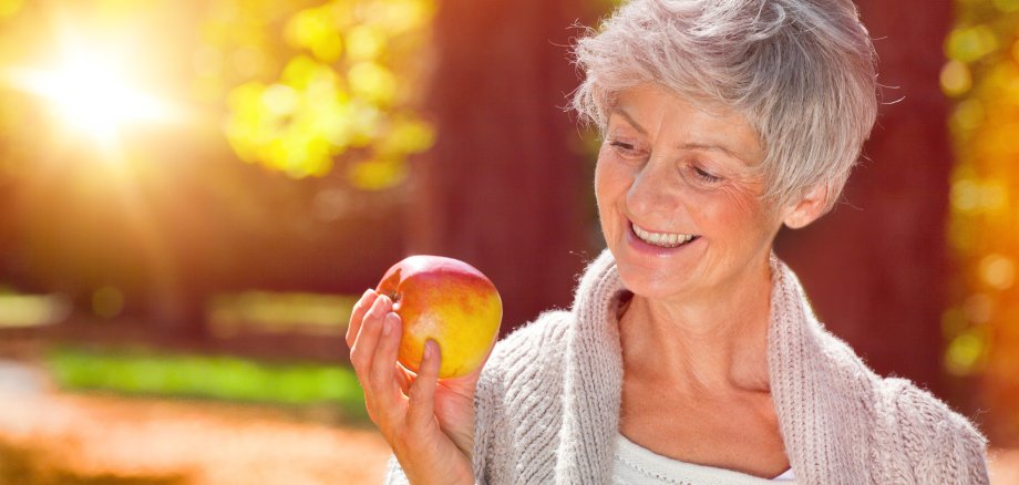 reife frau mit apfel Auf dem Bild sieht man eine lachende Frau, die einen Apfel in der Hand hält.