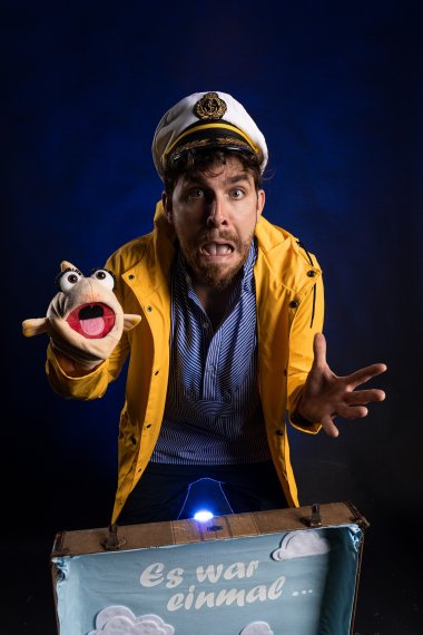 Auf dem Bild sieht man einen Theaterspieler mit einer Fischhandpuppe