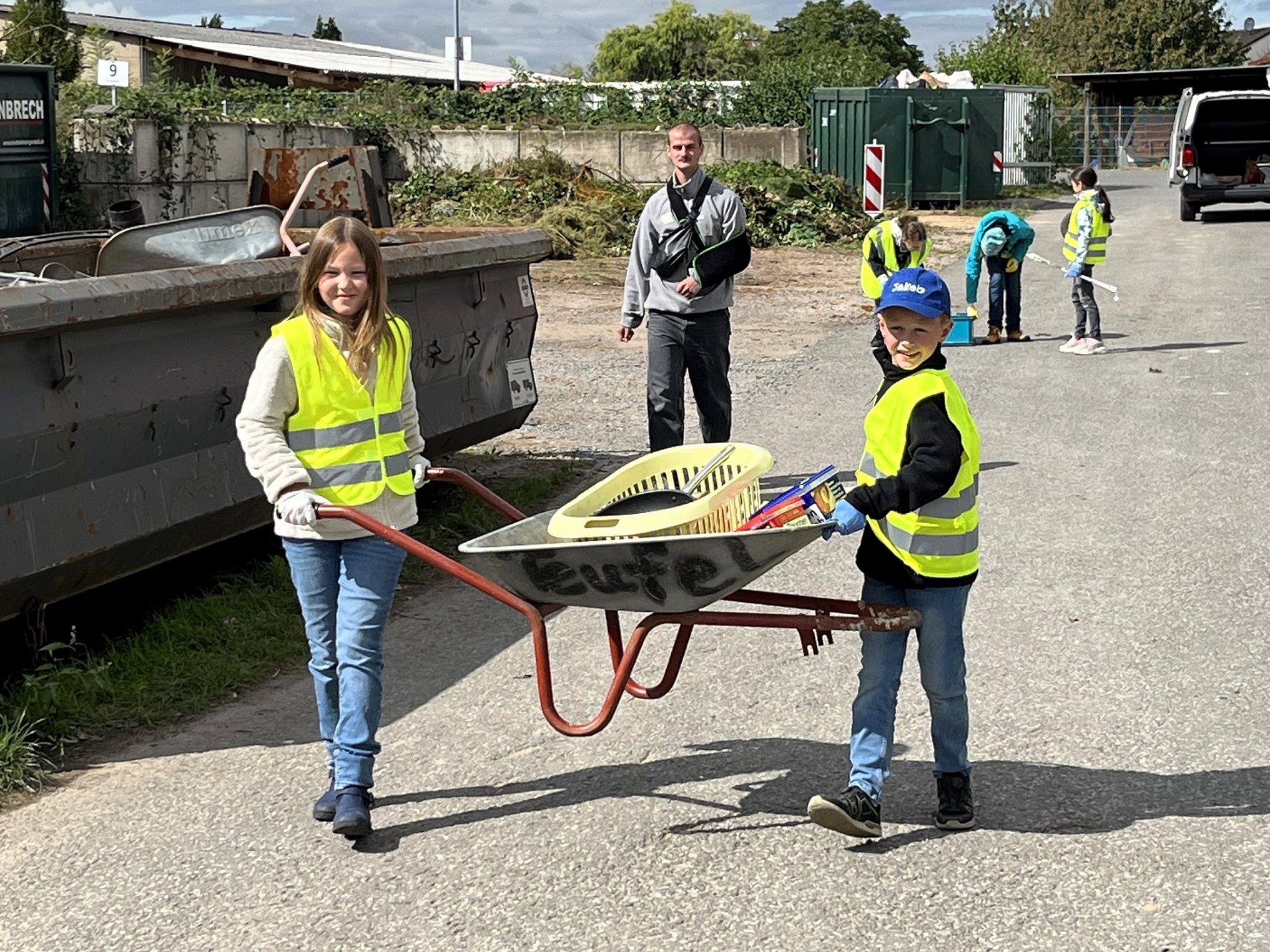 Man sieht 2 Kinder die eine Schubkarre tragen