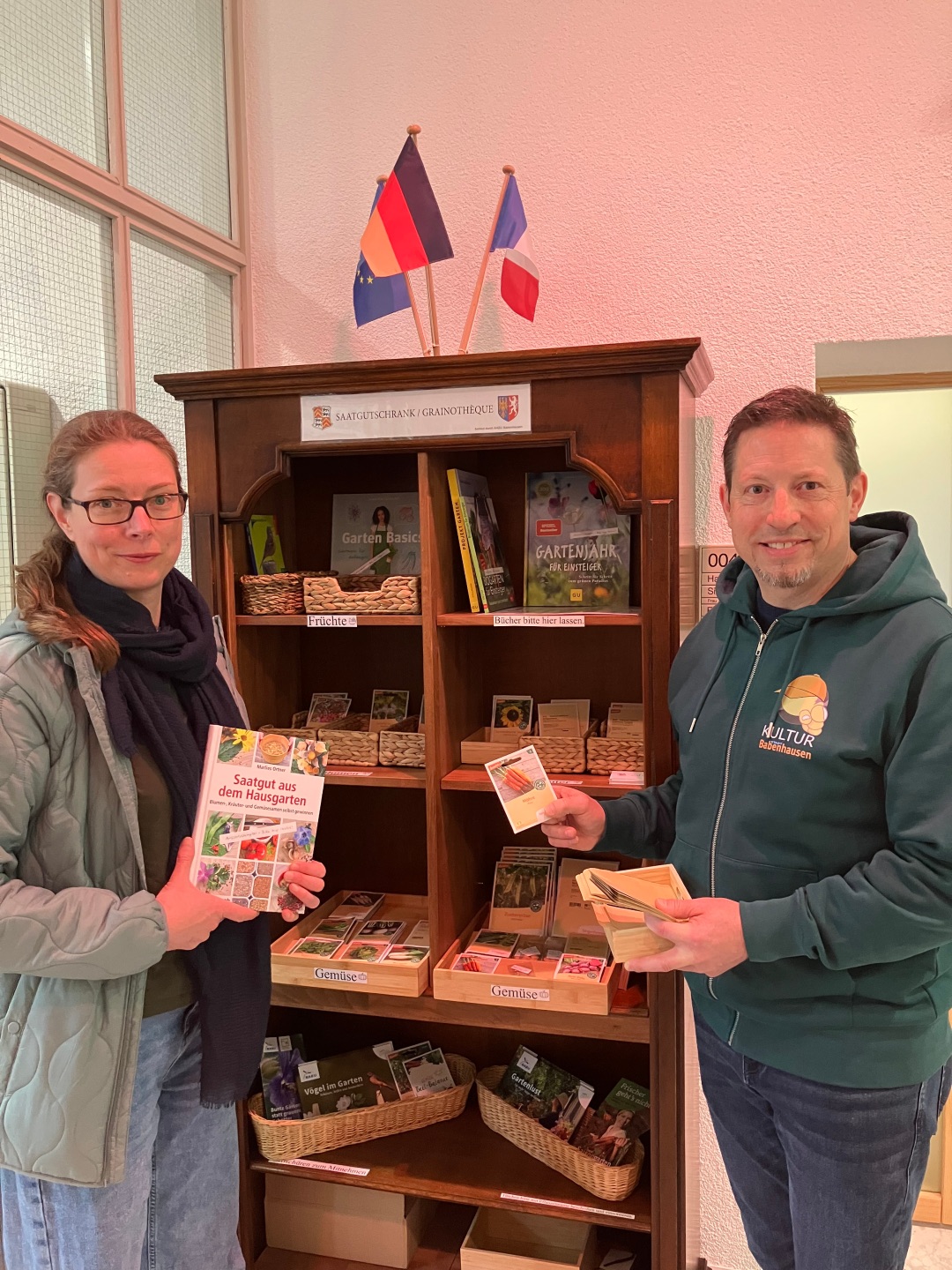Ulrike Gencarelle vom NABU Babenhausen und Michael Spiehl von der Stabsstelle JUGEND, SPORT & KULTUR beim Befüllen des Saatgutschrankes im Foyer des Rathauses.