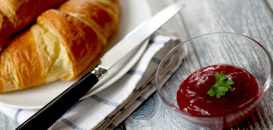 Man sieht ein Bild vom Seniorenfrühstück. Auf einem Tisch liegt ein Croissant und Marmelade