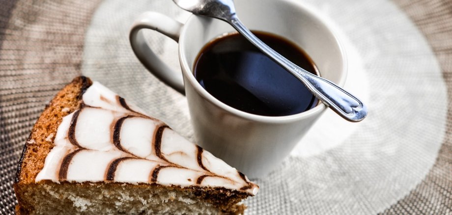 Man sieht ein Stück Kuchen mit einer Tasse Kaffee nebendran