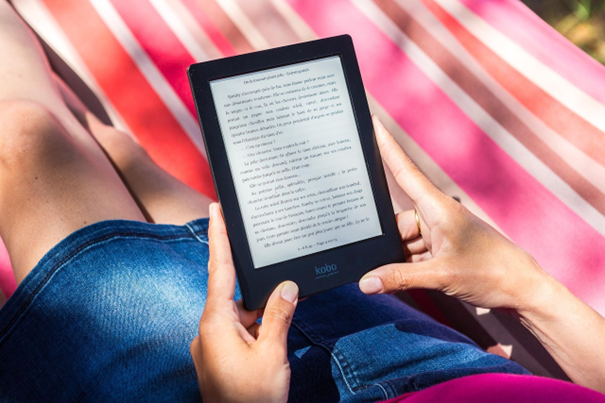 Person sitzt auf Strandtuch mit eReader in den Händen