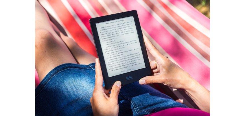 Person sitzt auf Strandtuch mit eReader in den Händen
