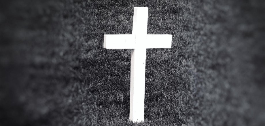Das Bild zeigt ein Kreuz auf einer Wiese in Schwarz Weiß