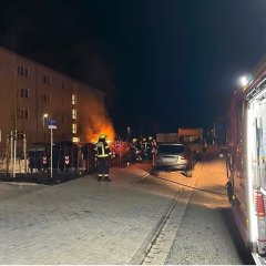 Auf dem Bild sieht man wie die Feuerwehrmänner eine brennende Hecke löschen. 