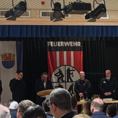 Man sieht mehrere Menschen auf der Bühne. Im Hintergrund hängt ein Banner von der Feuerwehr.