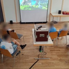 Auf dem Bild sieht man we die Kinder in der Stadthalle einen Film auf einer Leinwand schauen.