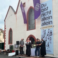 Auf dem Bild sieht man zwei Pfarrer und eine Pfarrerin vor der evangelischen Kirche.