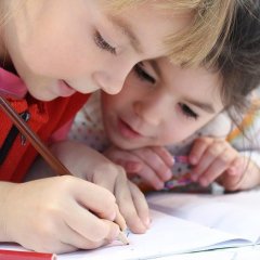 Auf dem Bild sieht man zwei Kinder die etwas in ein Heft schreiben. 