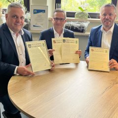 Auf dem Bild sieht man den Bürgermeister Dominik Stadler und zwei Männer von der Städtepartnerschaft Lichtentanne. Sie halten die Partnerschaftsurkunde hoch.