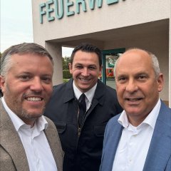 Man sieht den Bürgermeister Dominik Stadler und zwei Männer vor dem Feuerwehrhaus.
